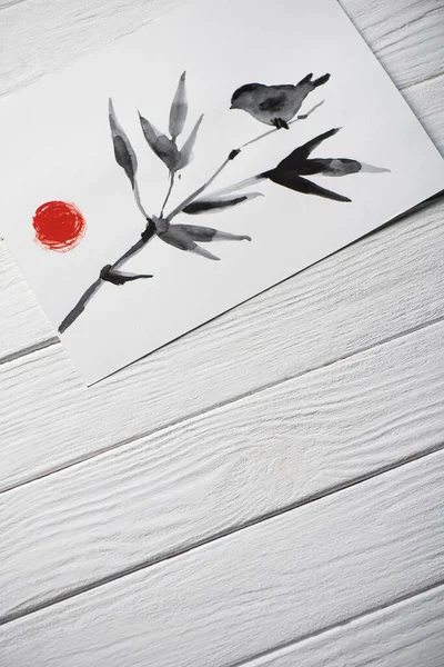 Vue du dessus du papier avec peinture japonaise avec oiseau sur branche avec feuilles et soleil sur fond en bois — Photo de stock