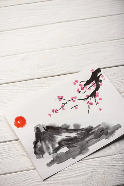 High angle view of paper with japanese painting with sun, Sakura branches and hill on wooden background — Stock Photo