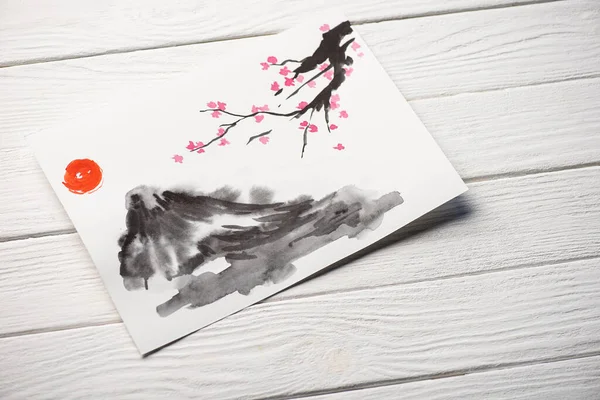 High angle view of paper with japanese painting with sun, Sakura branches and grey hill on wooden background — Stock Photo