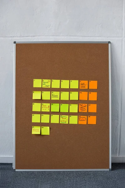 Panneau marron avec des notes collantes jaunes et orange près du mur — Photo de stock