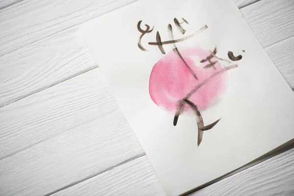 High angle view of paper with japanese painting with hieroglyphs on pink circle on wooden background — Stock Photo