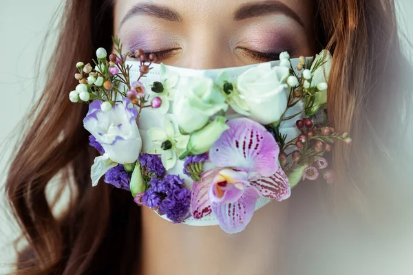 Mujer joven con los ojos cerrados en mascarilla floral aislada en gris - foto de stock