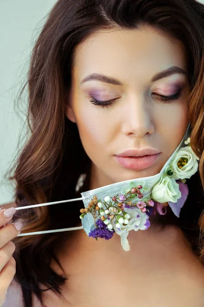Atractiva mujer tocando mascarilla con flores aisladas en gris - foto de stock