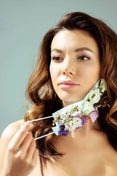 Schöne Frau berühren Gesichtsmaske mit Blumen isoliert auf grau — Stockfoto