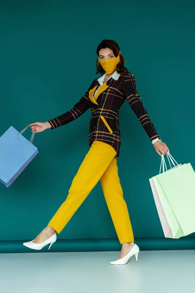 Elegante donna in maschera gialla e giacca a quadri che cammina con borse della spesa su blu — Foto stock