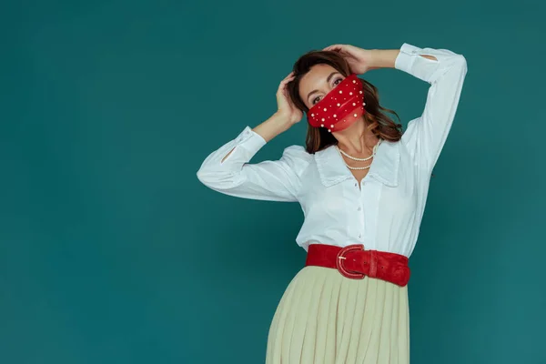 Стильна молода жінка в червоній масці торкається волосся ізольовано на синьому — стокове фото
