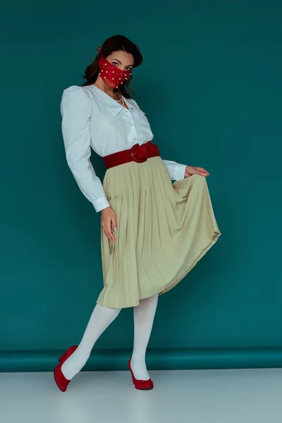 Élégant jeune femme en rouge masque toucher jupe sur bleu — Photo de stock