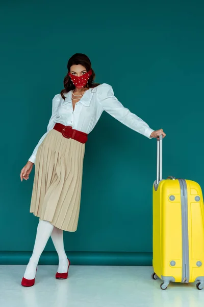 Стильна молода жінка в червоній масці позує з дорожньою сумкою на синьому — стокове фото