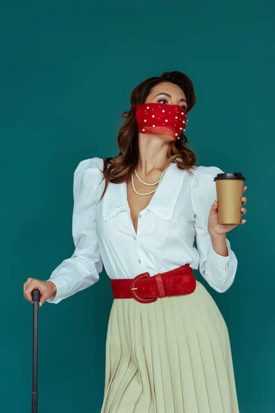 Chica con estilo en máscara roja celebración de café para ir aislado en azul - foto de stock