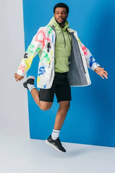 Homme afro-américain élégant posant dans un look futuriste coloré sur gris et bleu — Photo de stock