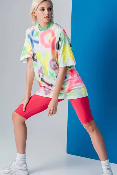 Fashionable woman posing in neon pink bike shorts and colorful t-shirt on grey and blue — Stock Photo