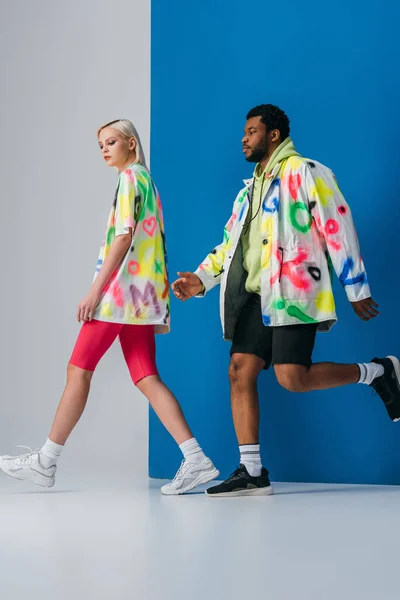 Stylish interracial couple posing in colorful futuristic look on grey and blue — Stock Photo