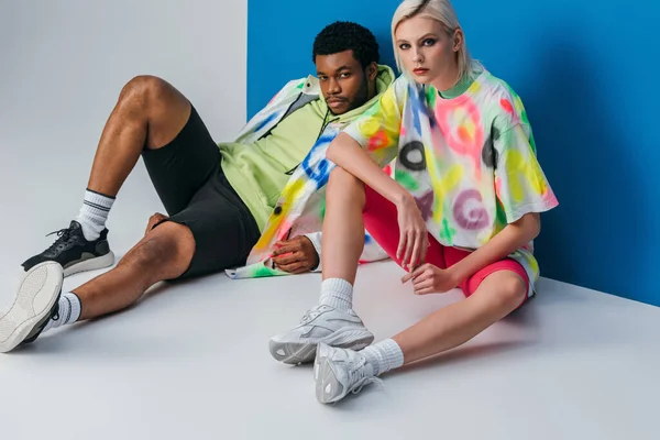 Fashionable interracial couple posing in colorful futuristic look on grey and blue — Stock Photo