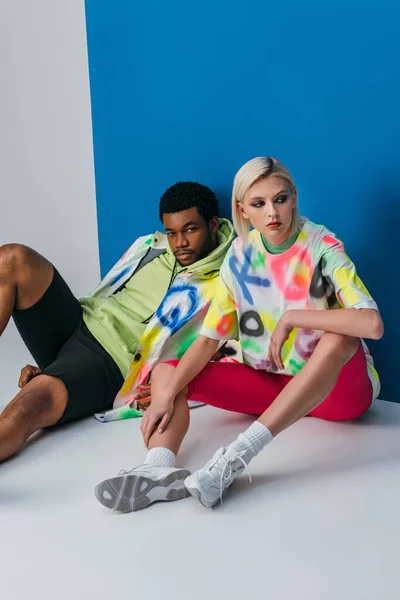 Couple multiculturel posant dans un look futuriste coloré sur gris et bleu — Photo de stock