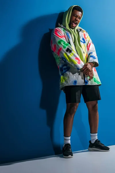 Excité élégant homme afro-américain criant et posant dans un look futuriste coloré sur gris et bleu — Photo de stock