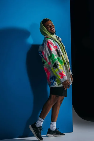 Fröhliche afrikanisch-amerikanische Mann posiert in bunten futuristischen Look auf grau und blau — Stockfoto