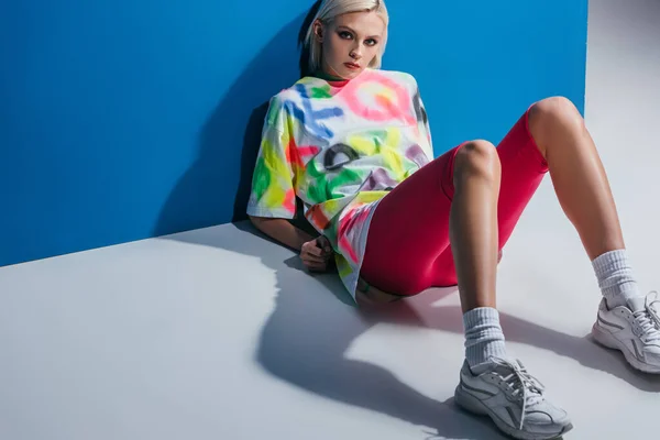 Stylish beautiful girl posing in neon pink bike shorts and colorful t-shirt on grey and blue — Stock Photo