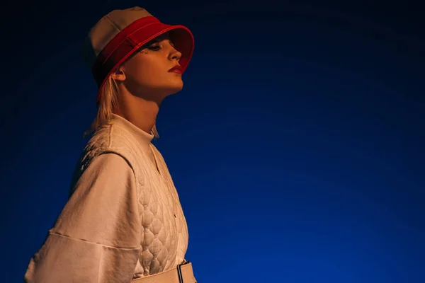 Modèle à la mode posant dans un look futuriste et chapeau sur bleu foncé — Photo de stock