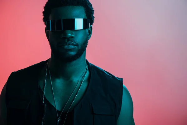 Young stylish african american man in futuristic sunglasses posing on pink in blue light — Stock Photo