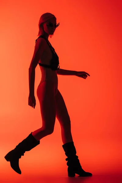 Chica futurista de moda posando en traje de cuerpo y gafas de sol en forma de fuego en rojo - foto de stock