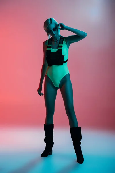 Model in futuristischem Trikot und feuerförmiger Sonnenbrille posiert auf rosa in blauem Licht — Stockfoto