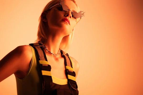 Attraente ragazza futuristica posa in occhiali da sole a forma di fuoco su arancione — Stock Photo