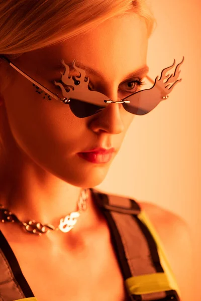 Stylish futuristic model posing in fire-shaped sunglasses on orange — Stock Photo