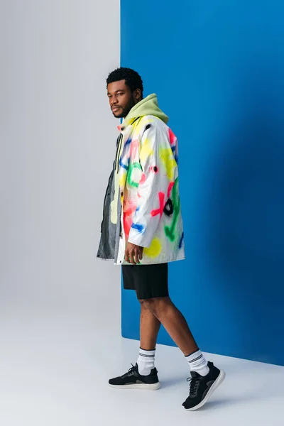 Uomo afroamericano in posa in abiti futuristici colorati su grigio e blu — Foto stock