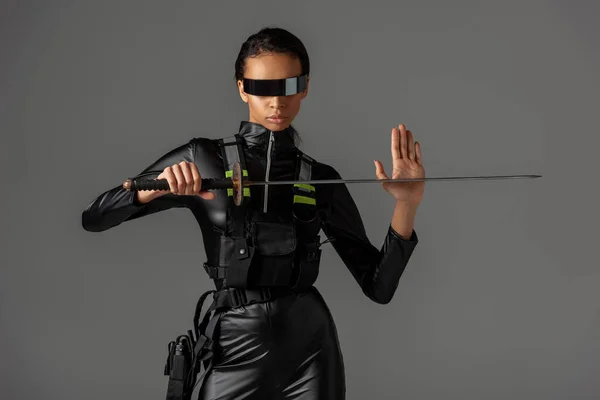 Séduisante femme afro-américaine futuriste dans des lunettes avec épée isolée sur gris — Photo de stock