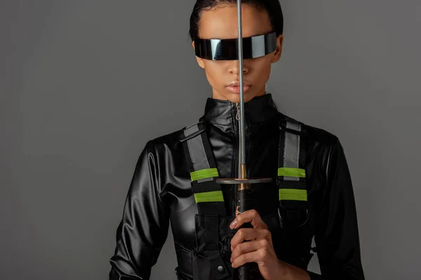 Atractiva mujer afroamericana futurista en gafas con espada aislada en gris - foto de stock