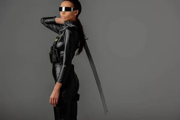 Visão lateral da mulher americana africana futurista em óculos com espada em cinza — Fotografia de Stock