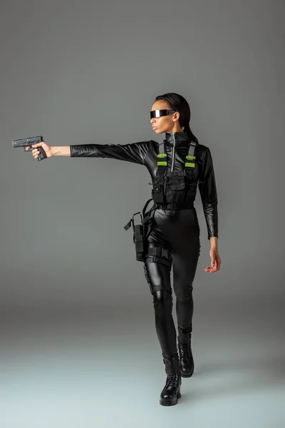 Attractive futuristic african american woman in glasses aiming gun on grey — Stock Photo