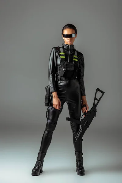Futuristische afrikanisch-amerikanische Frau mit Brille und Sturmgewehr auf grau — Stockfoto
