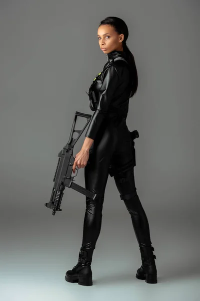 Futurista afroamericana mujer con rifle de asalto en gris - foto de stock