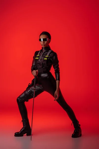 Attractive futuristic african american woman in glasses with sword on red background — Stock Photo