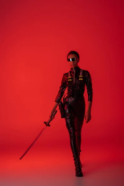 Futurista mujer afroamericana en gafas con espada sobre fondo rojo - foto de stock