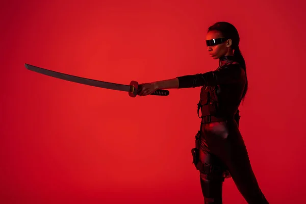 Futurista mujer afroamericana en gafas con espada sobre fondo rojo - foto de stock