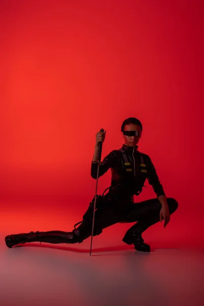 Futuriste afro-américaine dans des lunettes assis avec épée sur fond rouge — Photo de stock