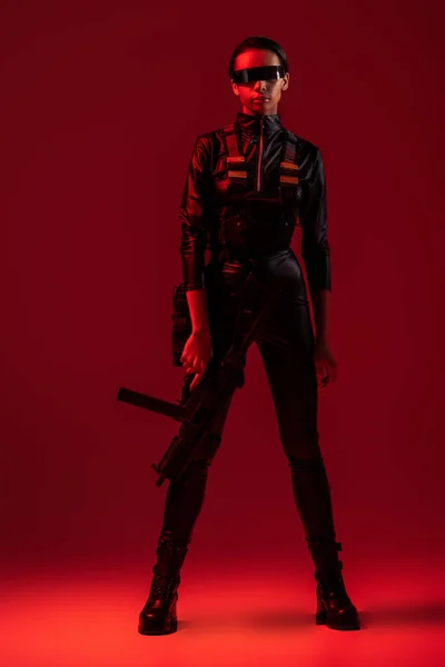 Futuristic african american woman in glasses with assault rifle on red background — Stock Photo