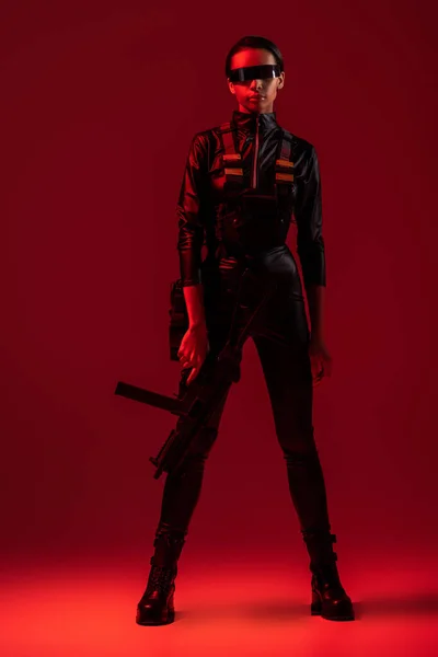 Futuristic african american woman in glasses with assault rifle on red background — Stock Photo