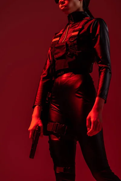Обрезанный вид на футуристическую африканскую женщину с пистолетом, изолированную на красном — стоковое фото