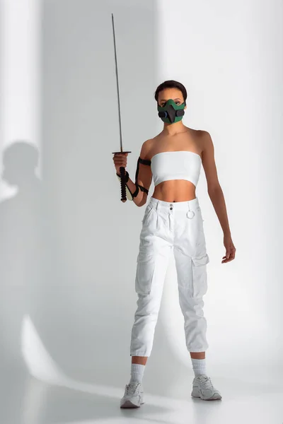 Futuristische afrikanisch-amerikanische Frau in Schutzmaske mit Schwert auf weißem Hintergrund — Stockfoto