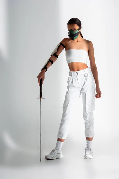 Futuristic african american woman in safety mask with sword on white background — Stock Photo