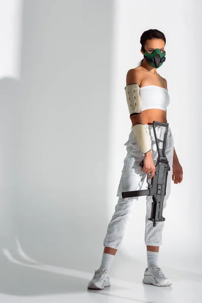 Futurista Africano americano mulher em máscara de segurança com rifle de assalto no fundo branco — Fotografia de Stock