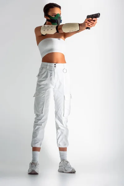 Futuristic african american woman in safety mask aiming gun on white background — Stock Photo