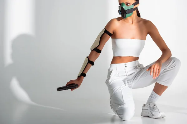 Futuristica donna afroamericana in maschera di sicurezza con pistola su sfondo bianco — Foto stock