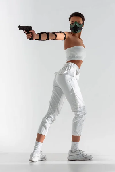 Futurista mulher afro-americana em máscara de segurança apontando arma no fundo branco — Fotografia de Stock