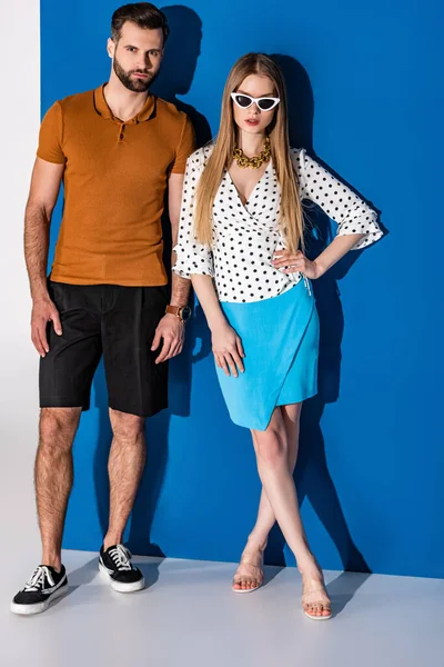 Stylish young couple posing in summer clothes and sunglasses on grey and blue — Stock Photo