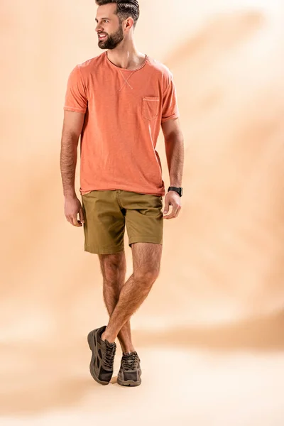Fröhlich stilvoller Mann posiert in Shorts und Sommer-T-Shirt auf beige — Stockfoto
