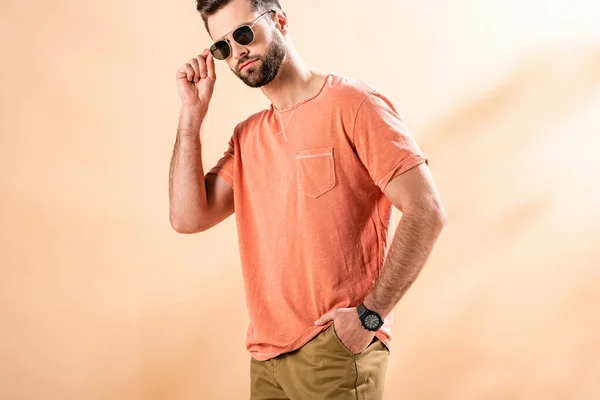 Stylish young man posing in shorts, summer t-shirt and sunglasses on beige — Stock Photo